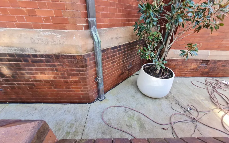 White surface deposits on a sandstone band above stained brickwork beside a downpipe.